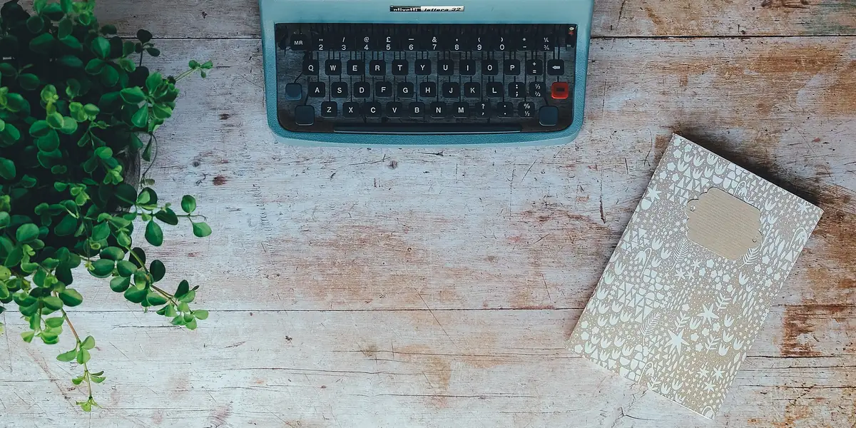 Vintage typewriter, notebook and green plant on a wooden desk, seen from above